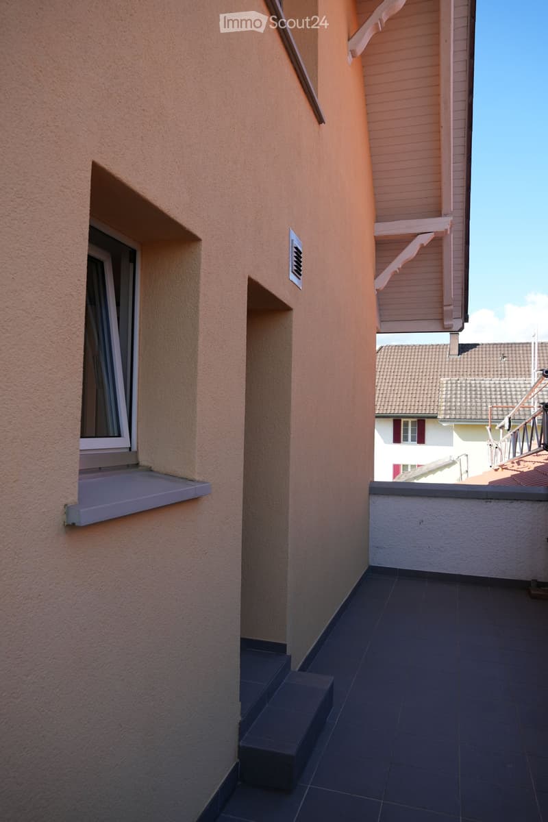 Balcony with dark tiled floor, steps leading up, window with white frame and awning, and a view of neighboring buildings.