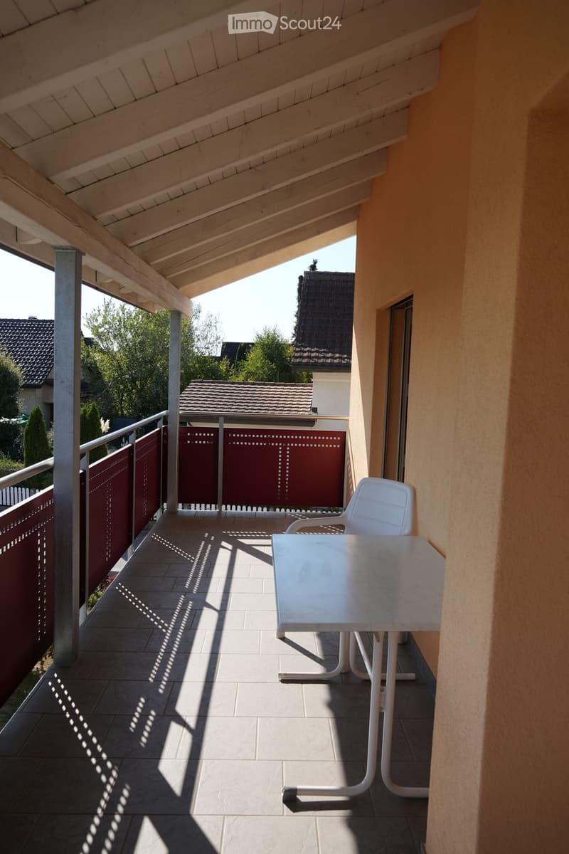 Balcony with a white table and chair, tiled floor, and red privacy screen.