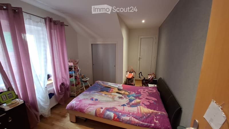 A cozy bedroom with a bed, nightstand, and a window with pink curtains. A baby stroller and chair are visible near the door.