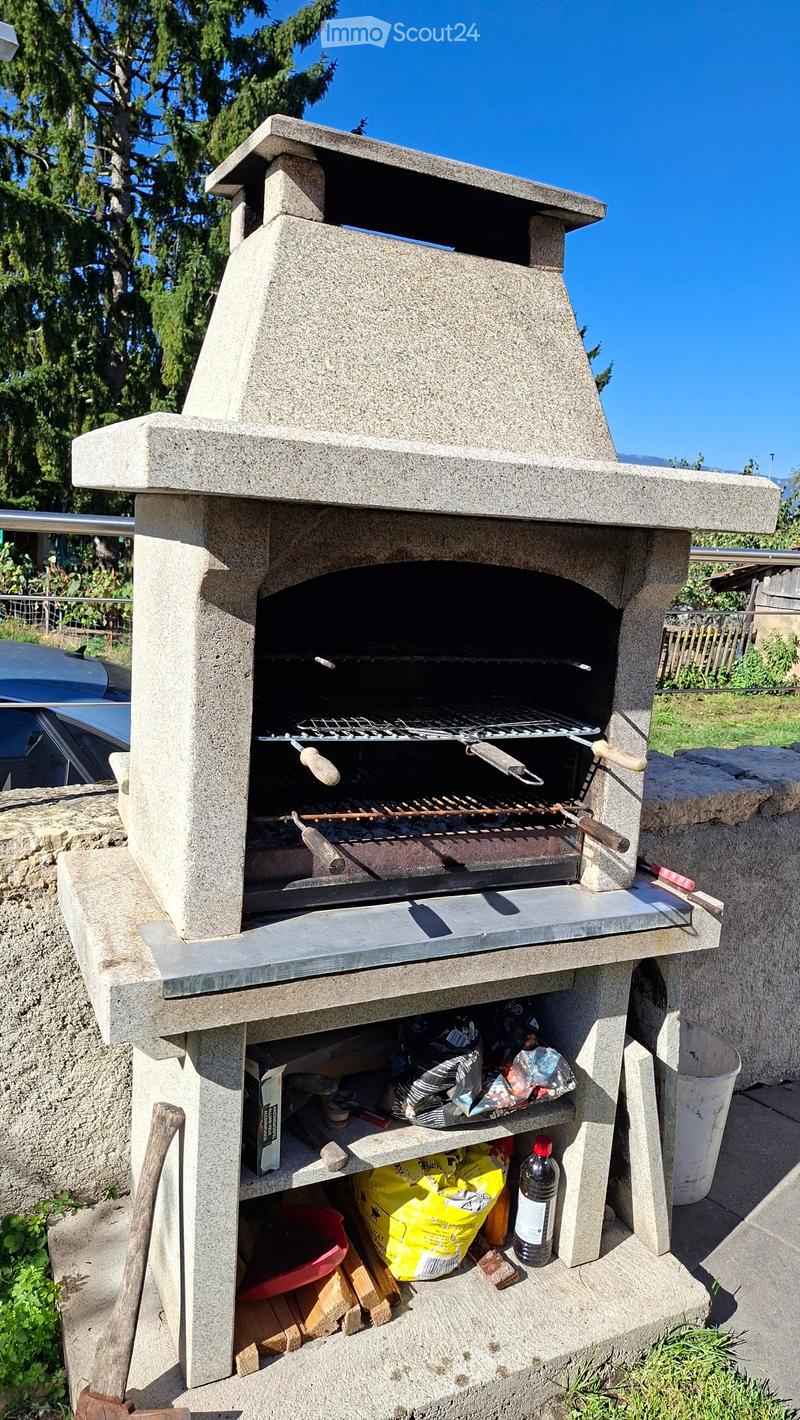 A stone outdoor pizza oven with a grill, storage space, and various items stored underneath.