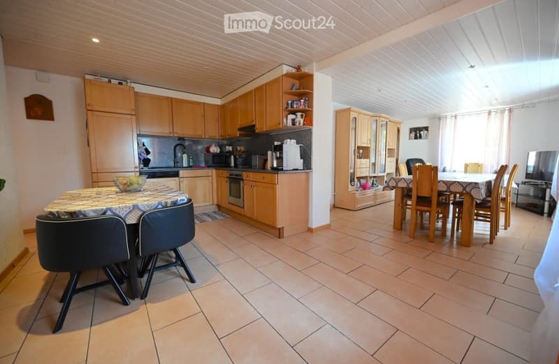 Bright, open-plan kitchen and dining area with wooden cabinets, stainless steel appliances, tiled floor, and a dining table with chairs.