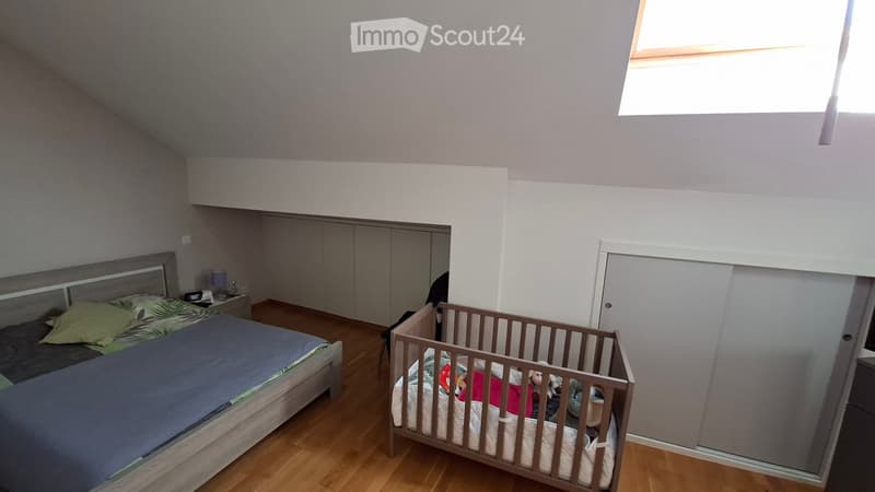 Bedroom with a double bed, crib, nightstand, lamp, and built-in wardrobe. The room features wooden flooring and a skylight window.