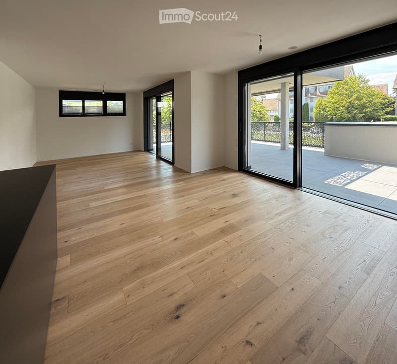 Empty room with light wooden flooring, large sliding glass doors leading to a balcony, and white walls.
