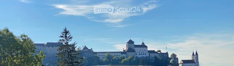 A historic castle with multiple towers and spires, surrounded by trees and a clear blue sky.