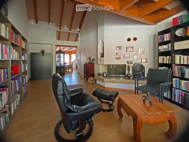 Cozy living room with wooden floors, fireplace, leather sofa, coffee table, bookshelf, and additional seating area visible in the background.