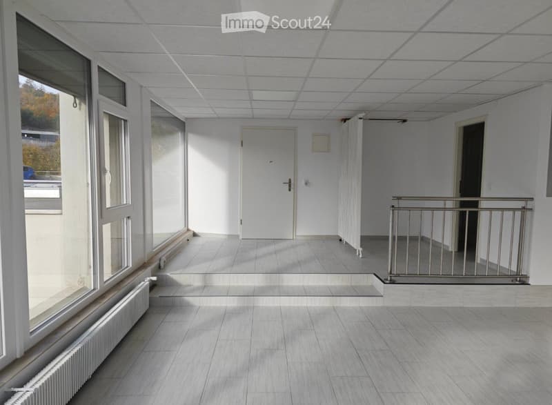 Empty hallway with tiled floor, white walls, large windows, and a metal railing leading to another area.