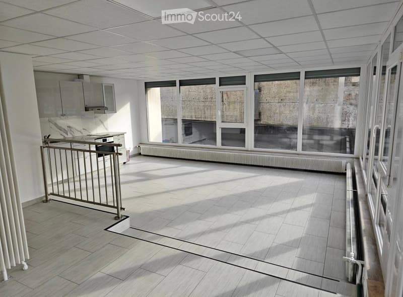 Empty room with tiled floor, white walls, large windows, and a metal railing. No furniture or equipment present.