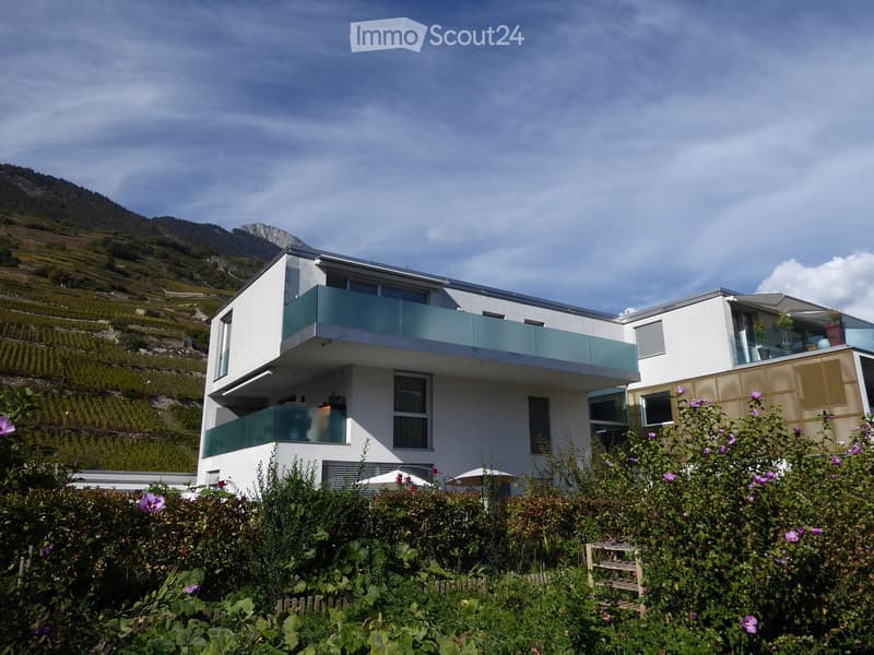 Modern two-story house with white walls, large windows, and a balcony overlooking a scenic mountain landscape.