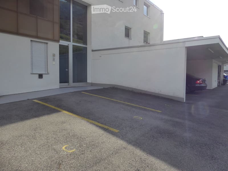 Modern building with a covered parking area, featuring large windows and a sleek design.