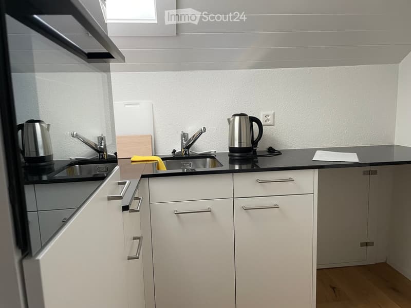 Modern kitchen with white cabinets, black countertops, stainless steel sink, and electric kettle.