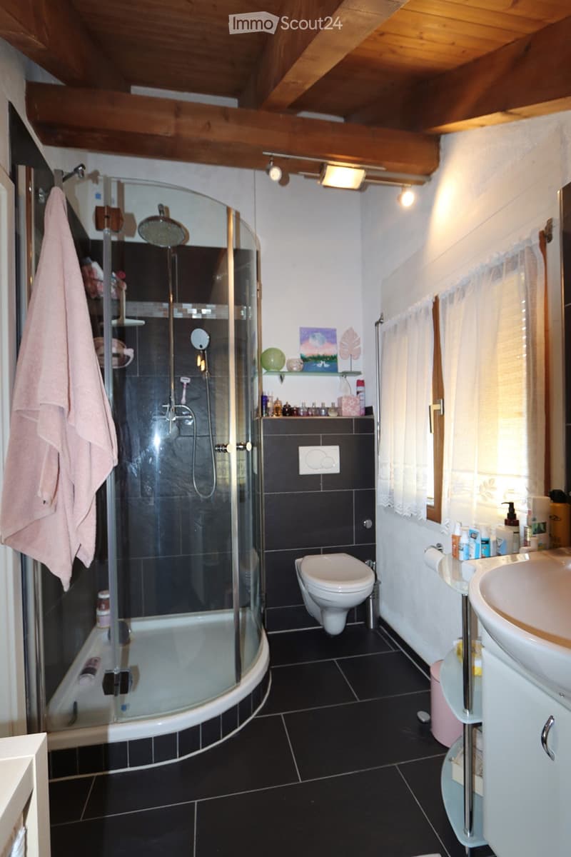 Bathroom with black tiles, a glass-enclosed shower, a toilet, a sink, and a towel hanging on the wall.