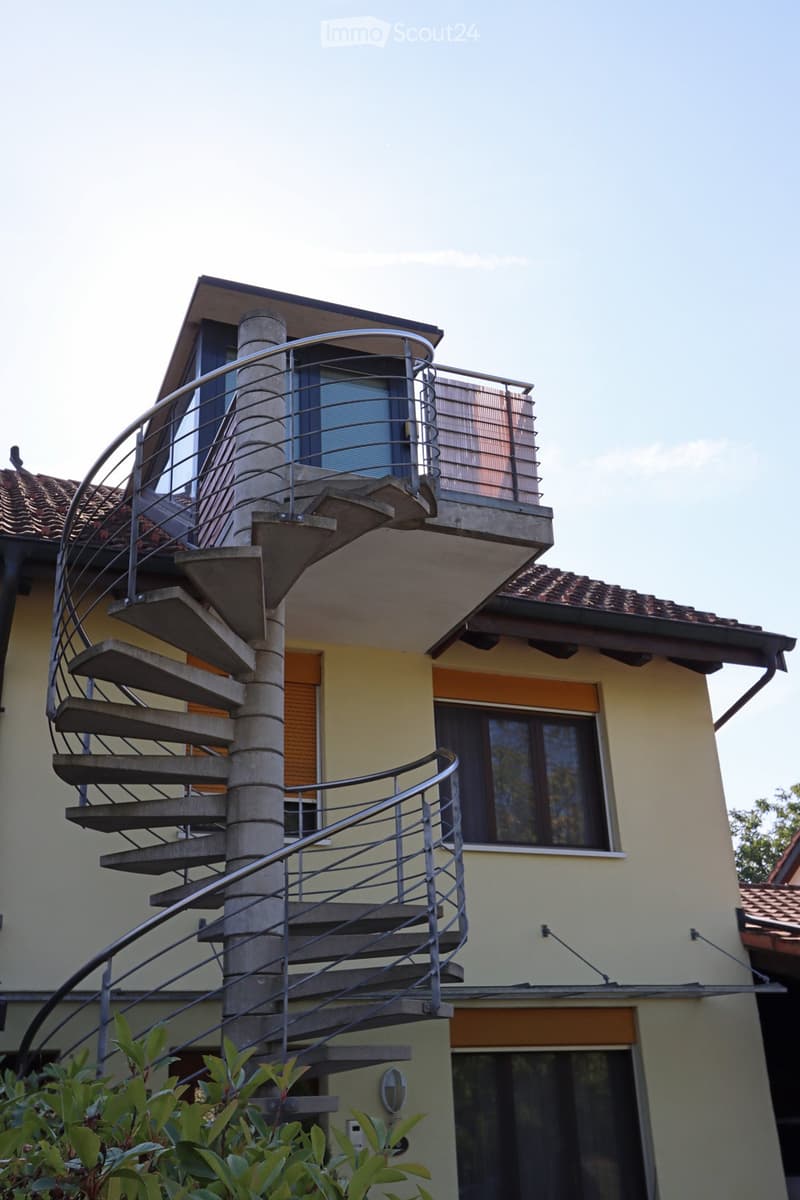 Two-story house with a modern spiral staircase leading to a rooftop terrace, featuring metal railings and concrete steps.