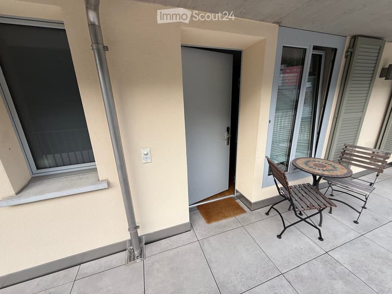 Balcony with tiled floor, small table, and two chairs, adjacent to a door and window.