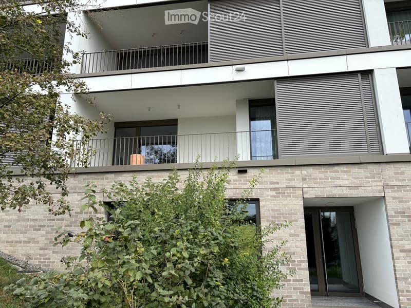 Modern multi-story residential building with balconies, large windows, and a brick lower level.