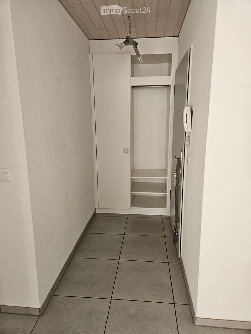 Empty hallway with tiled floor, white walls, built-in storage cabinet, and a phone mounted on the wall.
