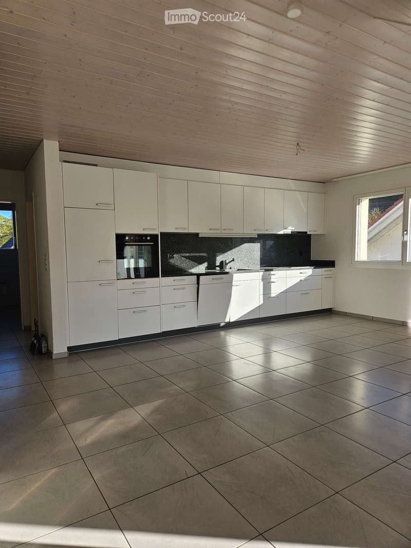 Modern kitchen with white cabinets, stainless steel oven, and tiled floor. Sunlight streams in from a window on the right.