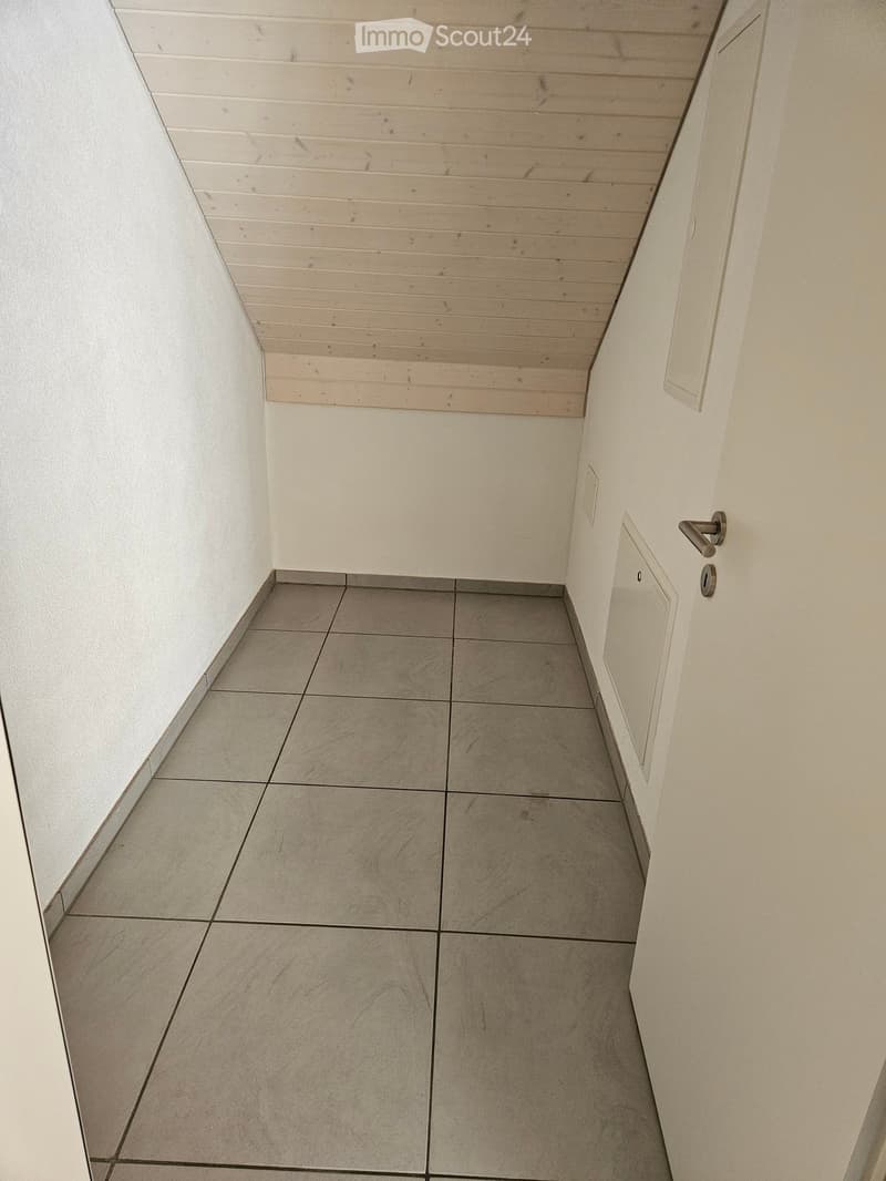 Empty hallway with tiled floor and white walls, featuring a door with a silver handle on the right side and a light switch on the left wall.