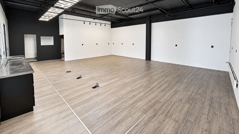 Empty room with wooden flooring, white walls, and a small black cabinet with a sink on the left side.