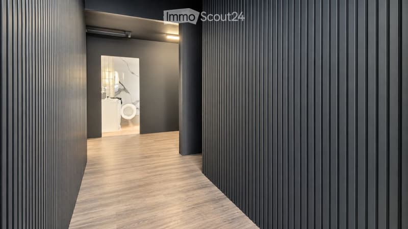 Modern hallway with dark grey walls, wooden flooring, and an open doorway leading to a bathroom.