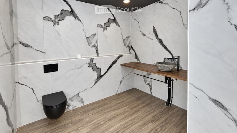 Modern bathroom with marble walls, wooden floor, black toilet, wooden sink, and a decorative sink bowl.
