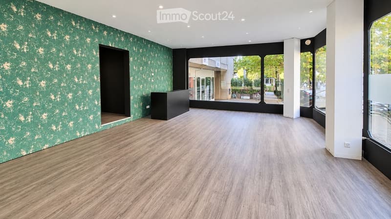 Empty room with wooden flooring, green textured wall, and large windows overlooking an outdoor area.
