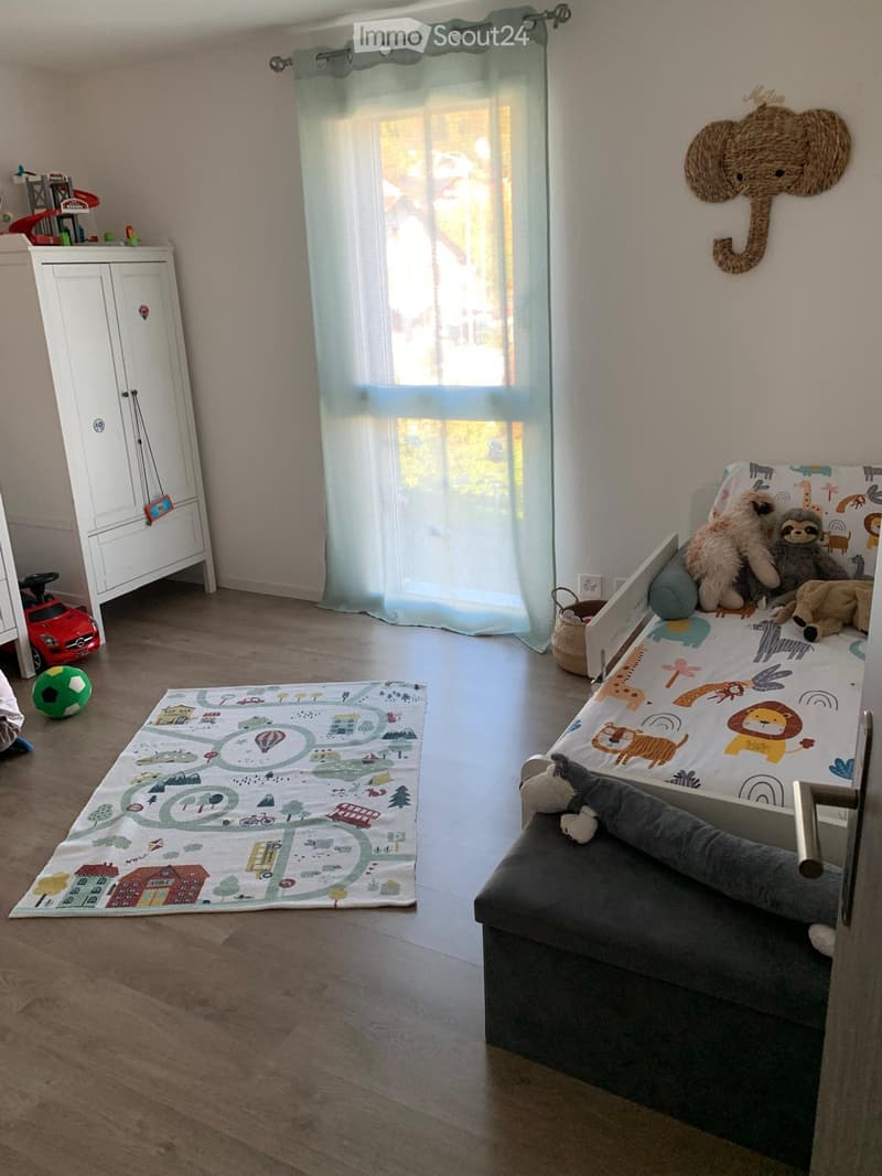 A well-lit children's bedroom with a bed, stuffed toys, a toy car, a ball, a rug, and a wardrobe.