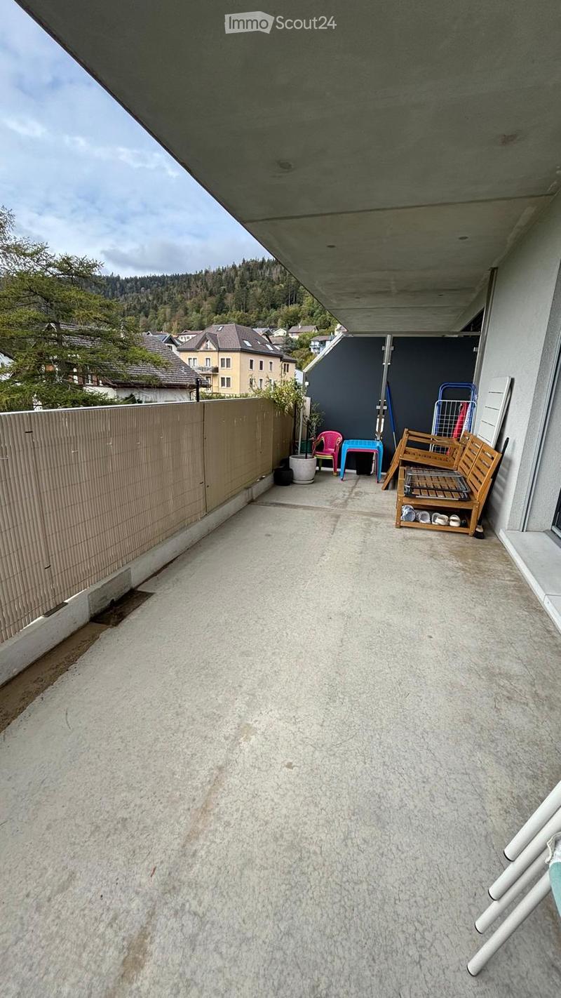 Balcony with concrete floor, wooden bench, small seating area with chairs and stools, potted plant, and storage unit.