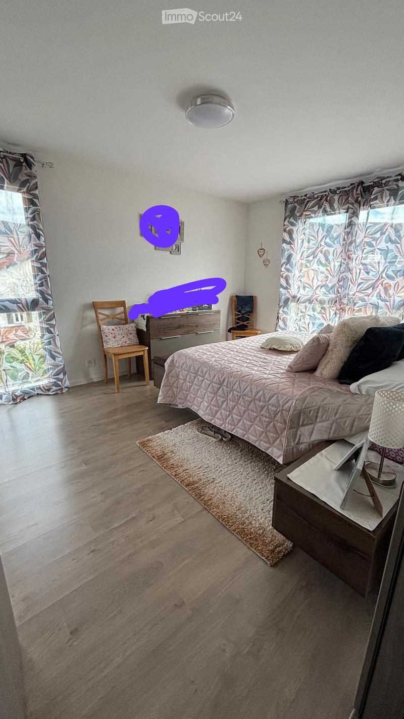 Cozy bedroom with a large bed, nightstand, chair, and decorative curtains. The room features wooden flooring and a soft area rug.