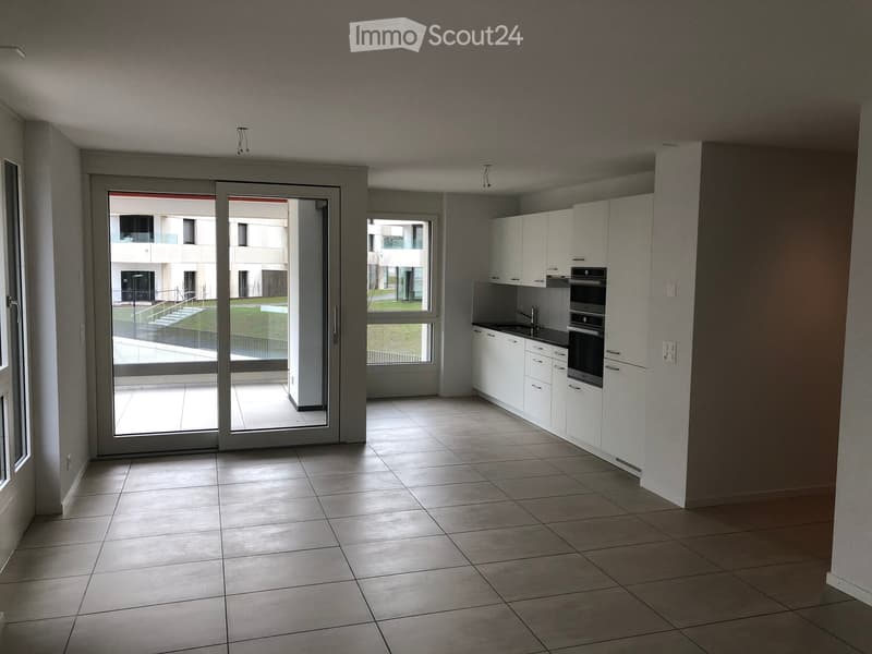 Empty kitchen with white cabinets, stainless steel appliances, tiled floor, and large sliding glass doors leading to a balcony.