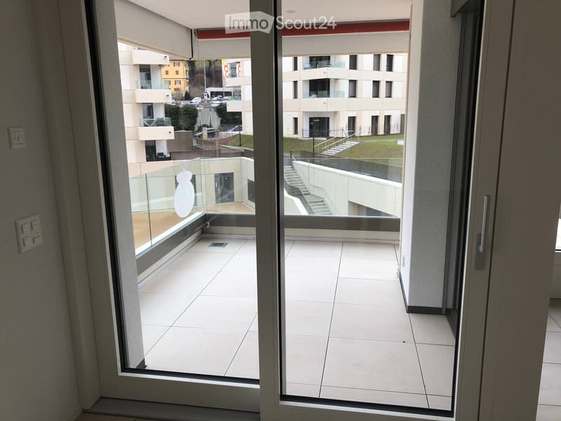Modern balcony with white tiled flooring, glass railing, and a view of a contemporary building complex with multiple levels and balconies.