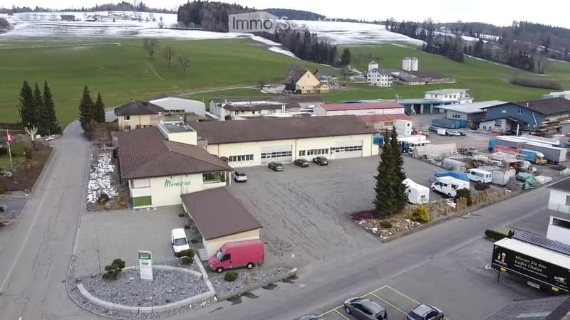 Aerial view of a commercial building complex with multiple structures, parking lot, and surrounding landscape.