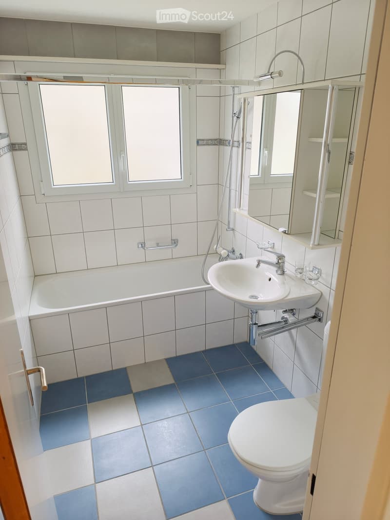 Modern bathroom with white tiles, blue floor tiles, bathtub, sink, toilet, and mirror.