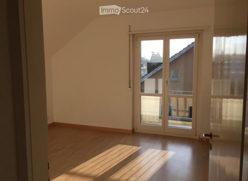 Empty room with wooden flooring, large sliding glass doors leading to a balcony, and natural light streaming in.
