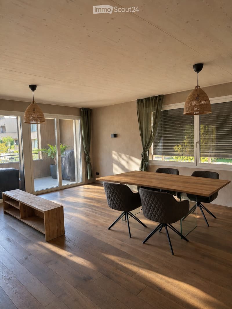 Modern dining area with wooden floor, large windows, and sliding glass doors leading to a balcony. Includes a wooden dining table, four black chairs, a wooden bench, and a dark-colored sofa.