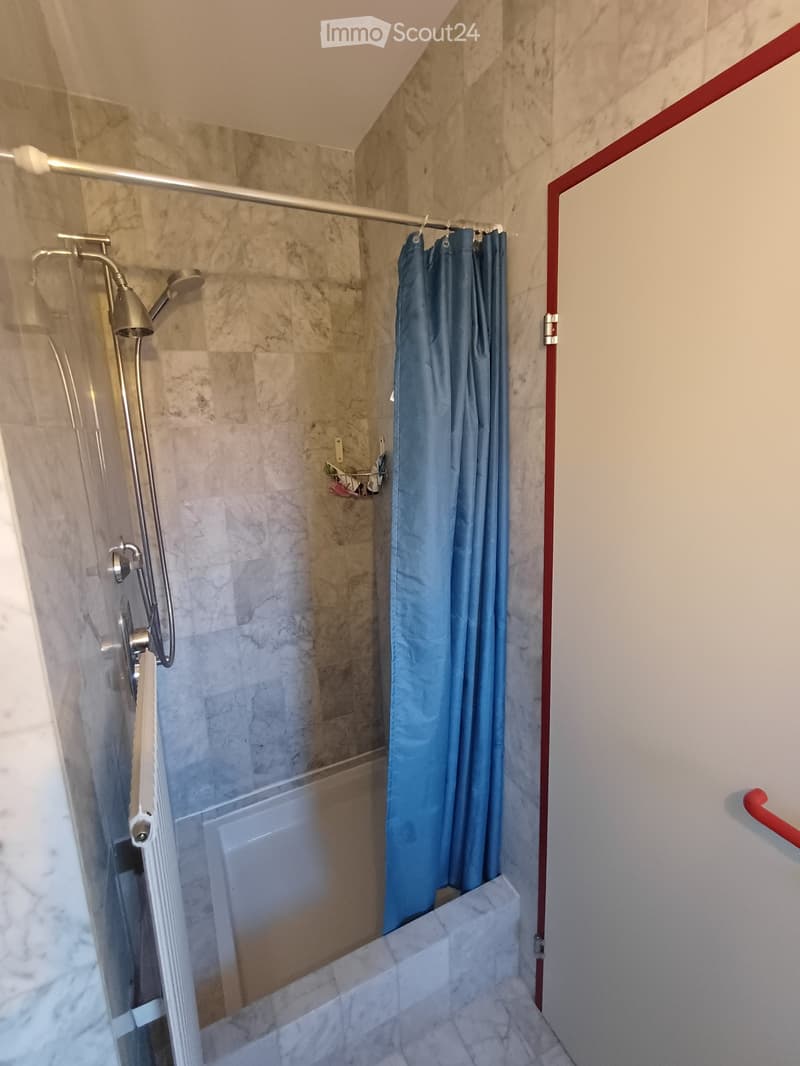 Modern bathroom with marble tiles, glass shower enclosure, and a blue shower curtain.