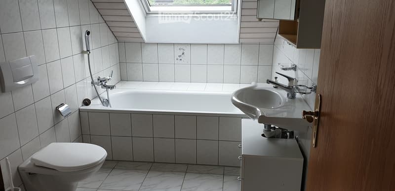 Modern bathroom with white tiles, a bathtub, a sink with a faucet, a toilet, and a mirror above the sink.