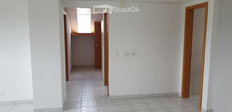 Empty hallway with white walls, tiled floor, and wooden doors leading to other rooms.