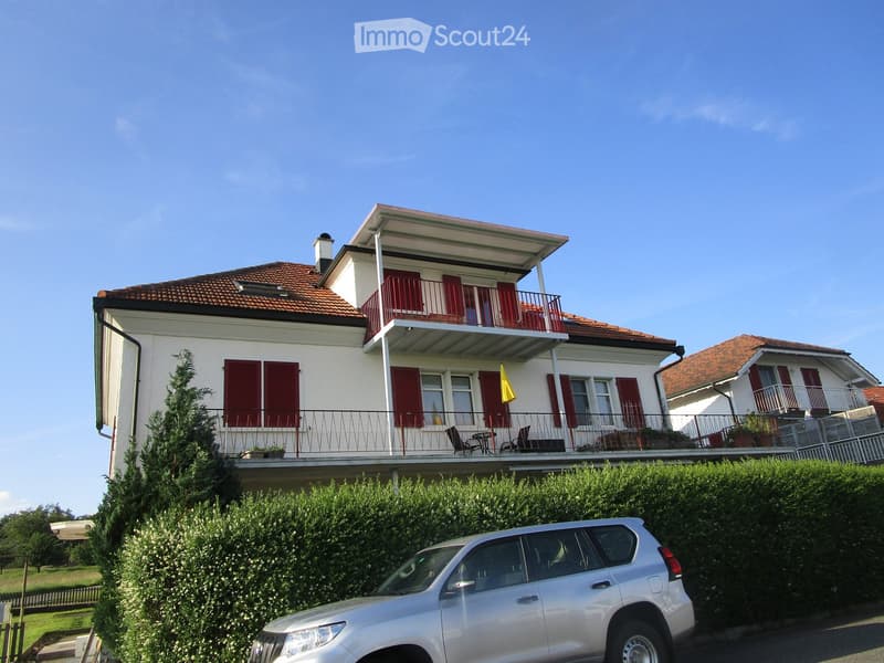 Two-story house with white walls, red shutters, and a balcony with outdoor furniture.