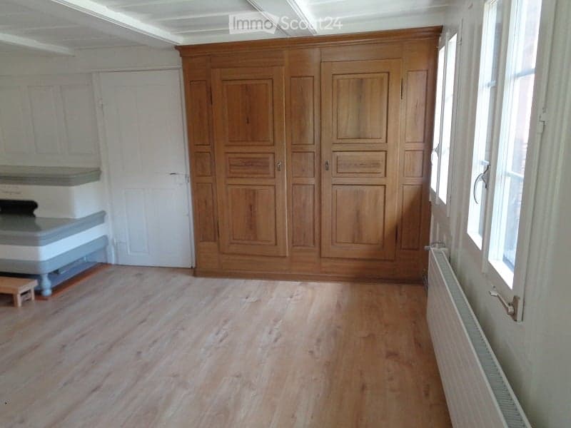 Empty room with wooden flooring, large wooden wardrobe, white walls, and windows. No furniture or equipment present.