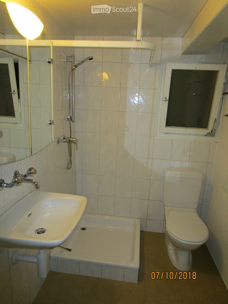 Bathroom with white tiled walls, a sink, a toilet, a bathtub, and a showerhead. The room has a window with frosted glass and a mirror above the sink.