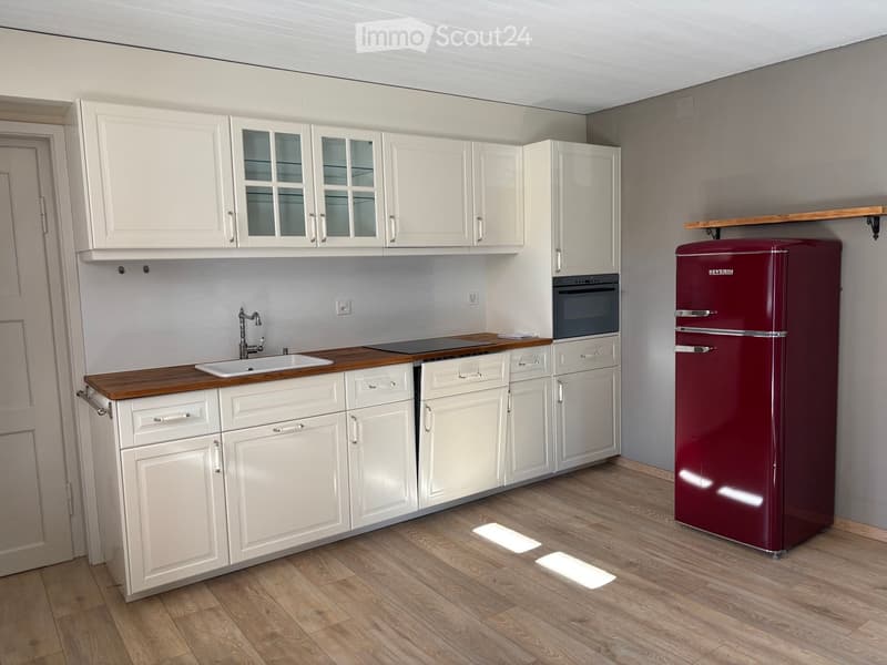 Modern kitchen with white cabinets, wooden countertops, a sink, faucet, oven, and a red refrigerator.
