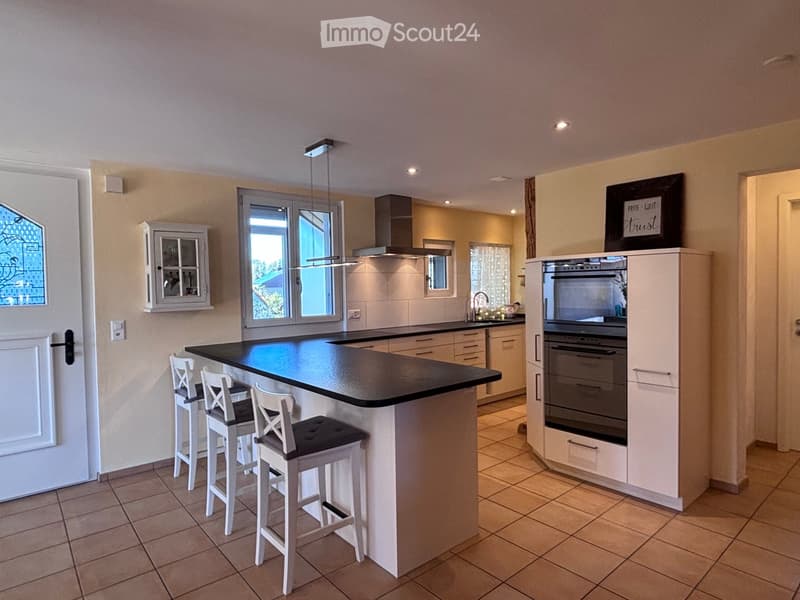 Modern kitchen with a central island, four white stools, built-in oven, and ample cabinetry.