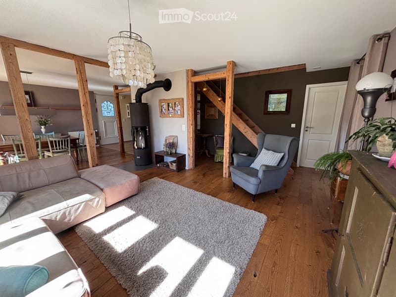 Living room with wooden flooring, a grey sofa, ottoman, armchair, coffee table, chandelier, fireplace, and plants.