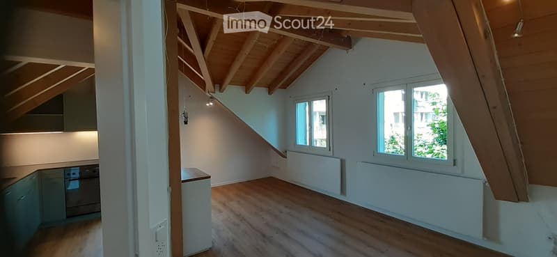 Bright, open attic space with wooden beams, wooden flooring, and large windows allowing natural light. The room is empty, with no furniture or equipment visible.