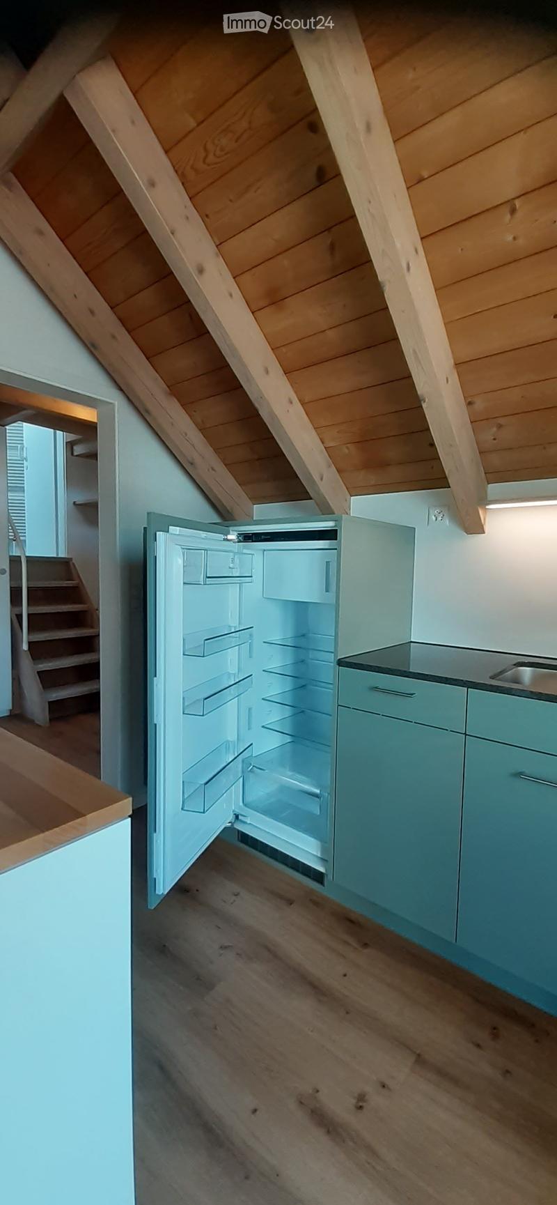 Modern kitchen with light blue cabinets, wooden flooring, and an open refrigerator with empty shelves.