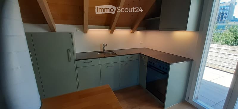 Modern kitchen with grey cabinets, a sink, a faucet, and an oven. The space features a wooden ceiling and a large window offering a view of greenery.