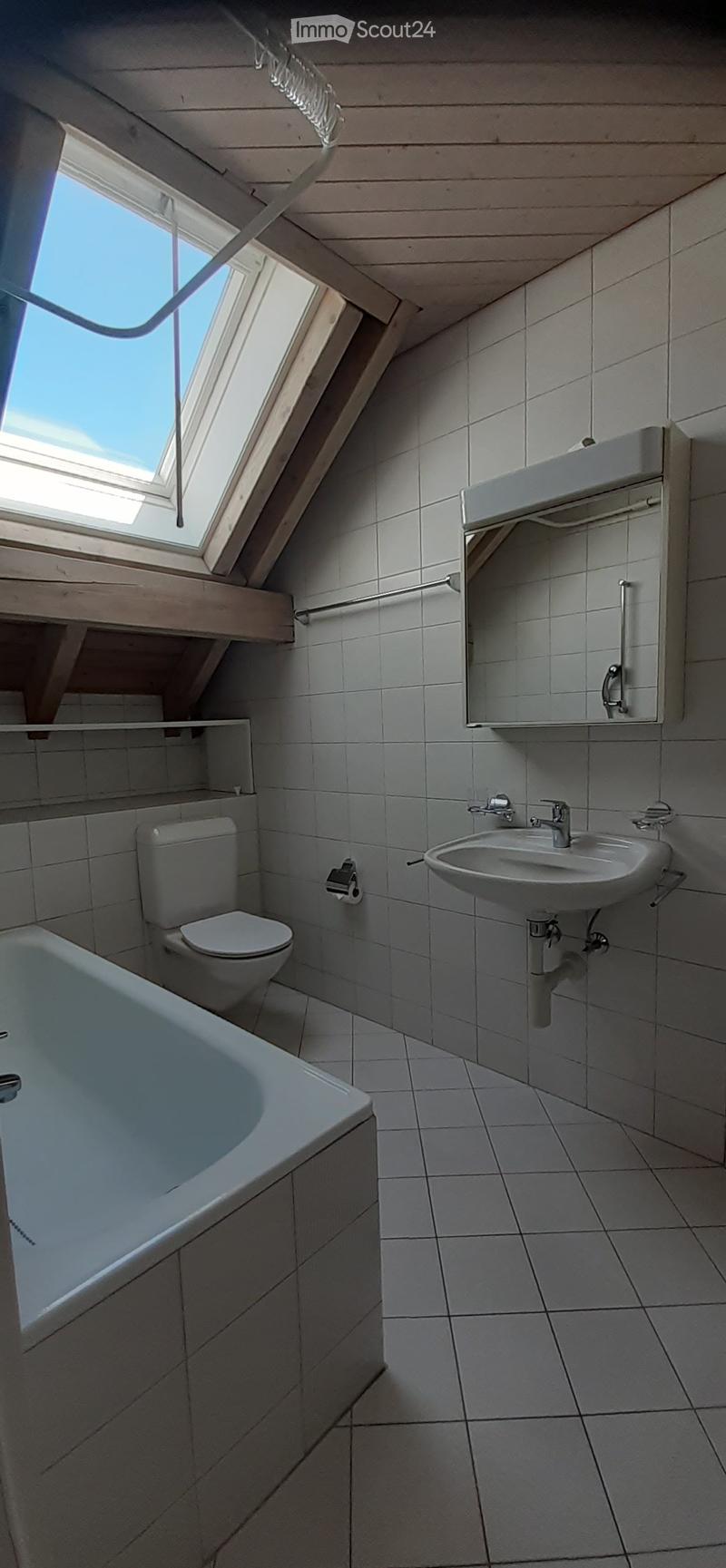Modern bathroom with white tiles, a bathtub, toilet, sink, mirror, and built-in cabinet. Features a skylight window for natural light.