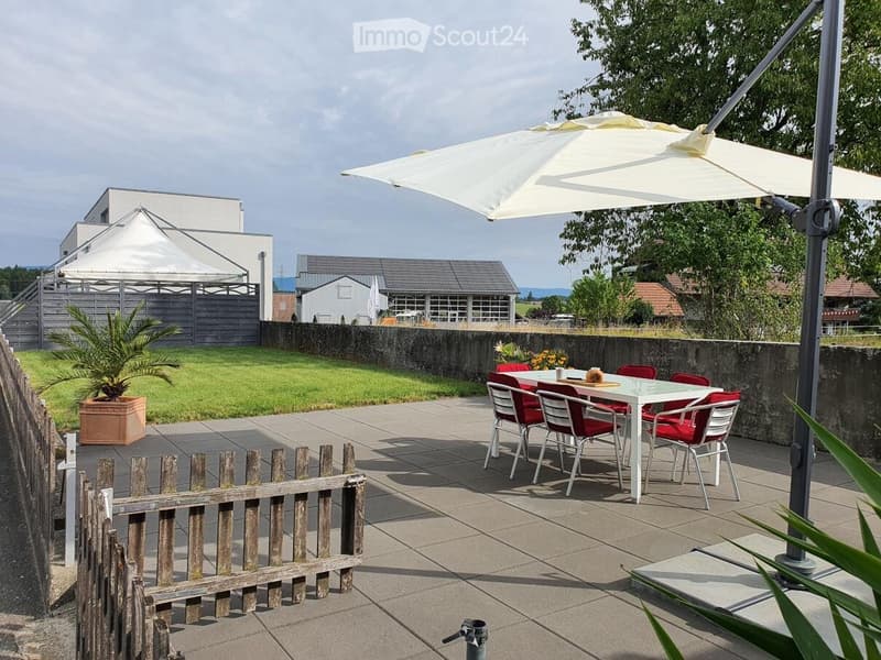 Outdoor patio with a white dining table, red chairs, umbrella, potted plant, and wooden fence.