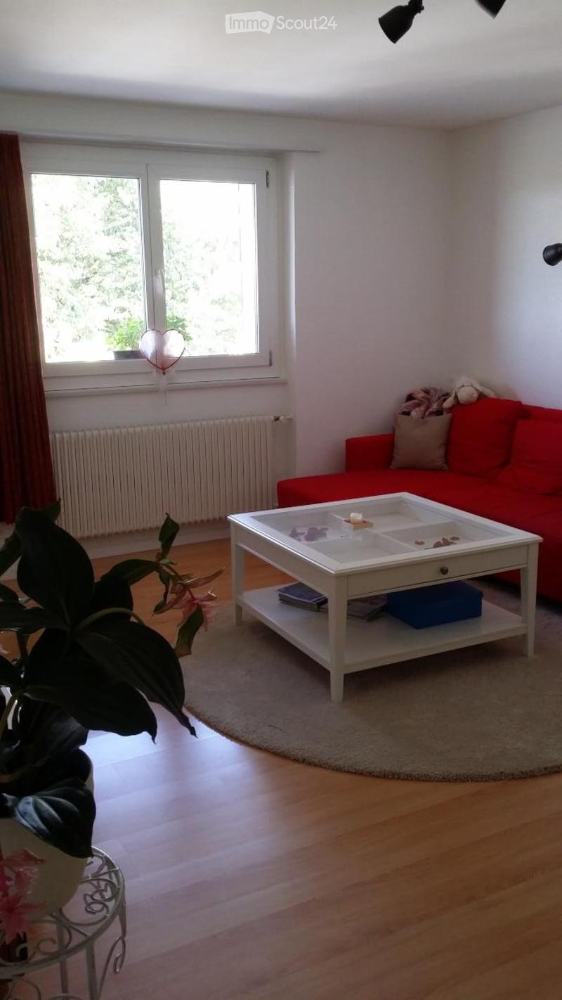 A cozy living room with a red sofa, a small white table, a plant, and a lamp near the window.