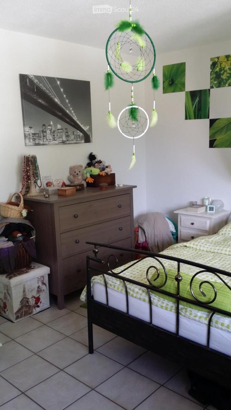 A cozy children's bedroom with a metal-framed bed, a wooden wardrobe, a large mirror, dreamcatchers, toys, and a basket on the shelf.
